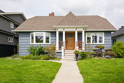 Residential house with concrete pathway to the main entrance over lush front yard lawn.