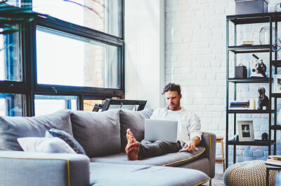 Man on couch in New York City apartment researches financial requirements for a co-op in NYC.