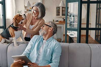 Happy senior couple in casual clothing smiling and taking care of their dog