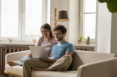 A couple looking at a laptop, resting on sofa at home.