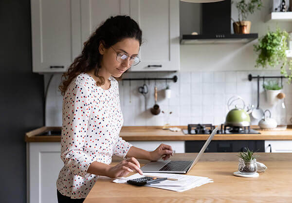 A homeowner at a kitchen island on a laptop researching income calculation for the home loan process.