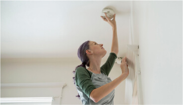 Woman checks smoke detector to maintain home safety.